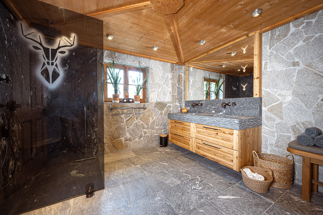 Chalet Badezimmer. grauer Duschwand. Rustikaler Naturstein mit Eichen Altholz