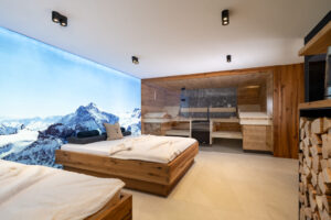 Wellness-Relax-Bett aus Eiche, dahinter eine Fotoleinwand mit winterlicher Berglandschaft. Altholz-Sauna aus Fichte mit rauem grauen Naturstein