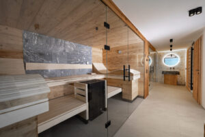 Altholz-Sauna aus Fichte mit rauem grauen Naturstein. Dampfsauna und begehbare schwarze Regendusche mit Fliesen aus Muschelperlmutt