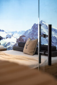 Wellness-Relax-Bett aus Eiche mit Leinenkissen und Hirschmotiv, dahinter eine Fotoleinwand mit winterlicher Berglandschaft.