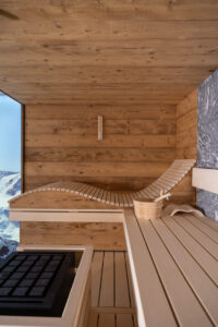 Altholz-Sauna aus Fichte mit rauem grauen Naturstein und Fotoleinwand mit winterlicher Berglandschaft.