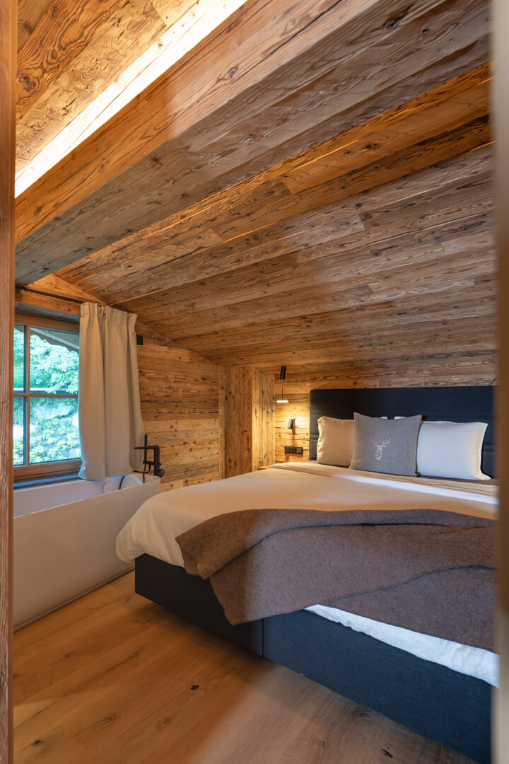 Gemütliches Schlafzimmer mit Altholzdecke und Verkleidung, Eckbadewanne, Kingsize-Bett und Swarovski-Hirschkissen.
