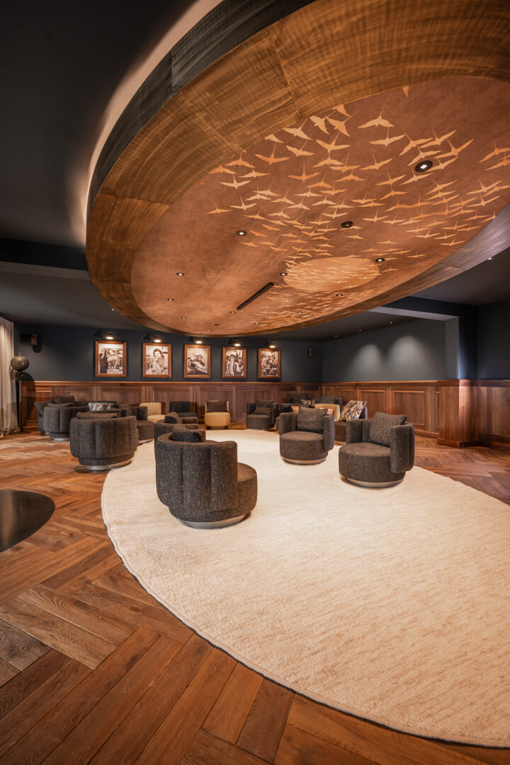 Elegantes Kaminzimmer, Fischgrätboden, Holz-Lambrisierung an den Wänden im englischen Stil sowie einem beleuchteten Decken-Centerpiece mit Vogelmotiv als Eyecatcher.