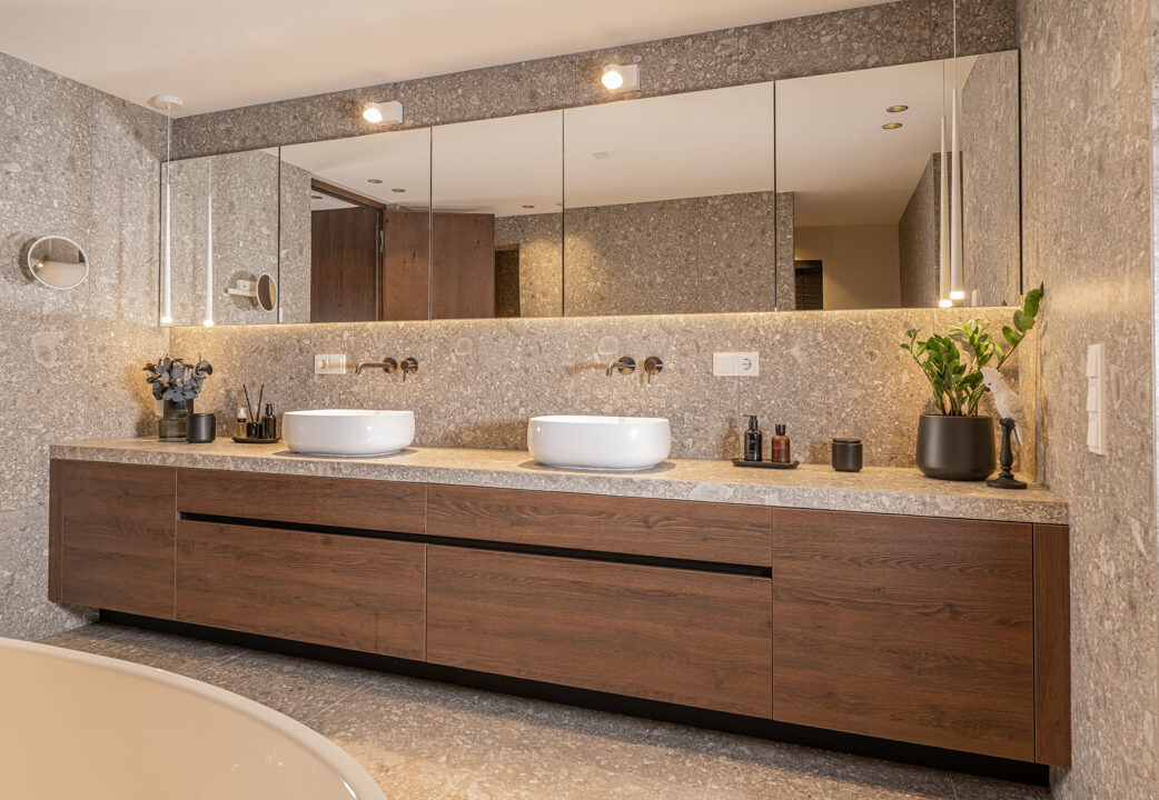 Badezimmer mit dunkelbraunem Holz-Waschtisch, marmorierten Naturstein-Look-Fliesen in Ivory.