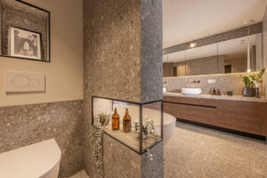 Badezimmer mit marmorierten Naturstein-Look-Fliesen in Ivory, dunkelbraunem Holz-Waschtisch, Trendwand zur Toilette.