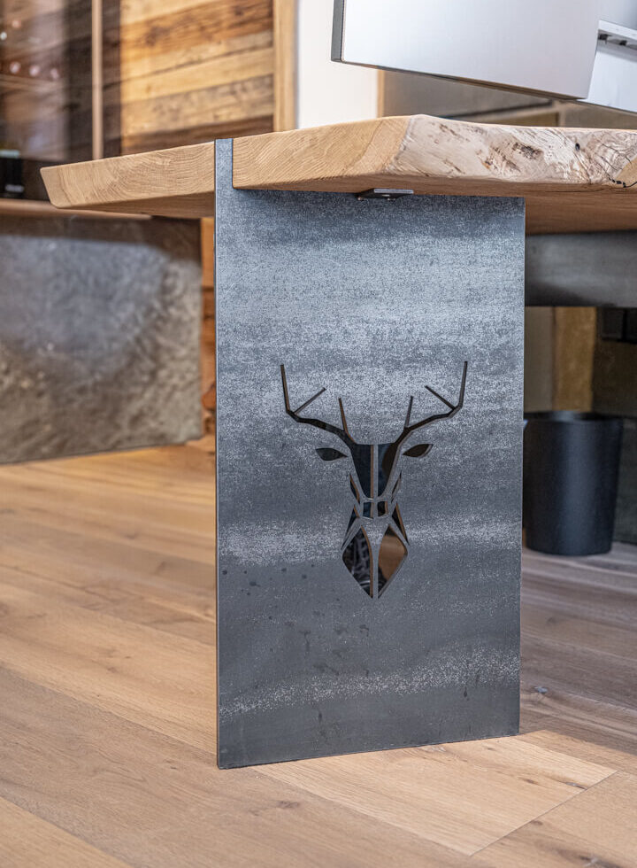Schreibtisch mit massiver Holzplatte auf Stahlfuß mit Hirschmotiv.